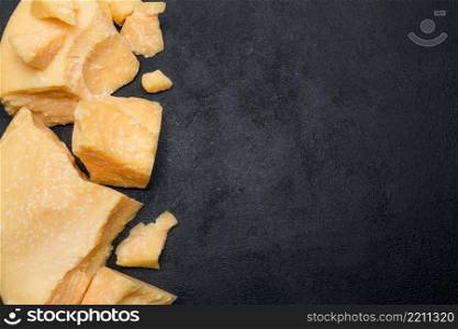 pieces of parmesan or parmigiano hard cheese on dark concrete background. pieces of parmesan or parmigiano cheese