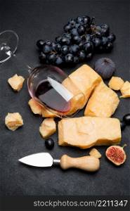 pieces of parmesan or parmigiano hard cheese, wine and grapes on dark concrete background. pieces of parmesan or parmigiano cheese, wine and grapes