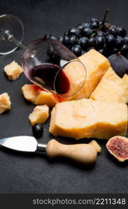 pieces of parmesan or parmigiano hard cheese, wine and grapes on dark concrete background. pieces of parmesan or parmigiano cheese, wine and grapes