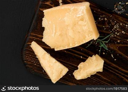 Pieces of parmigiano cheese on a cutting board. Top view of hard cheese on a dark background.