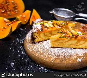 pieces of pumpkin pie on a wooden board sprinkled with powdered sugar, next to a fresh pumpkin