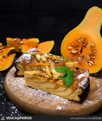 pieces of pumpkin pie sprinkled with powdered sugar on a wooden board, behind the fresh pieces of pumpkin