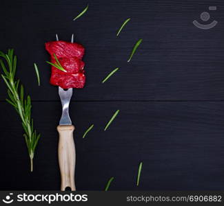 pieces of raw beef on kitchen fork with plastic handle on a black background, an empty space on the right