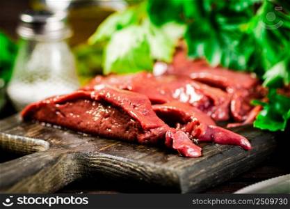 Pieces of raw liver on a cutting board with parsley and spices. On a wooden background. High quality photo. Pieces of raw liver on a cutting board with parsley and spices.