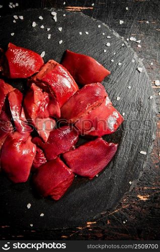 Pieces of raw liver on a stone tray with salt. Against a dark background. High quality photo. Pieces of raw liver on a stone tray with salt. 