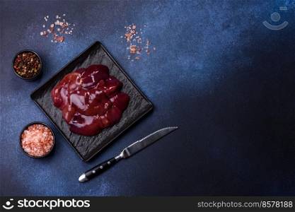 Pieces of raw liver on a wooden cutting board against a dark concrete background. Preparation of liver pate. Pieces of raw liver on a wooden cutting board against a dark concrete background