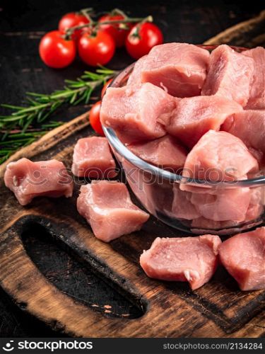 Pieces of raw pork in a glass bowl with tomatoes and rosemary. Against a dark background. High quality photo. Pieces of raw pork in a glass bowl with tomatoes and rosemary.