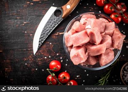 Pieces of raw pork in a glass bowl with tomatoes and rosemary. Against a dark background. High quality photo. Pieces of raw pork in a glass bowl with tomatoes and rosemary.