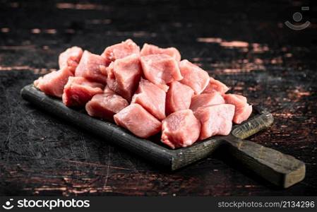 Pieces of raw pork on a cutting board on the table. On a rustic dark background. High quality photo. Pieces of raw pork on a cutting board on the table.