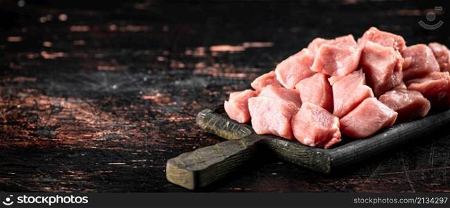 Pieces of raw pork on a cutting board on the table. On a rustic dark background. High quality photo. Pieces of raw pork on a cutting board on the table.