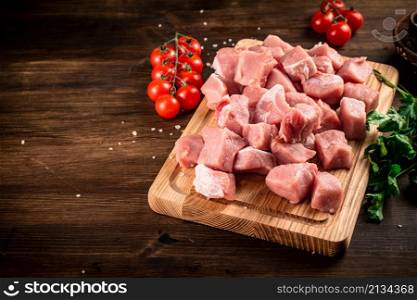 Pieces of raw pork on a cutting board with parsley and tomatoes. On a wooden background. High quality photo. Pieces of raw pork on a cutting board with parsley and tomatoes.