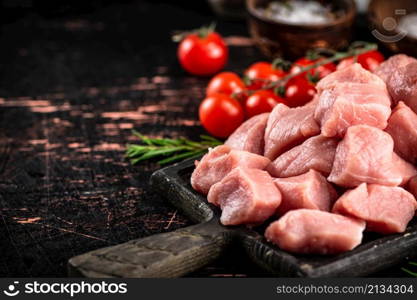 Pieces of raw pork on a cutting board with spices, tomatoes and rosemary. On a rustic dark background. High quality photo. Pieces of raw pork on a cutting board with spices, tomatoes and rosemary.