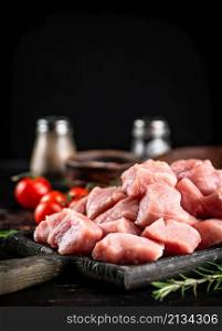 Pieces of raw pork on a cutting board with spices, tomatoes and rosemary. On a rustic dark background. High quality photo. Pieces of raw pork on a cutting board with spices, tomatoes and rosemary.