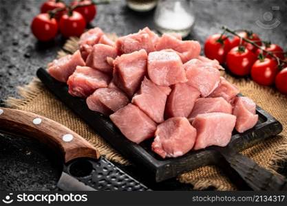 Pieces of raw pork on a cutting board with tomatoes. On a black background. High quality photo. Pieces of raw pork on a cutting board with tomatoes.