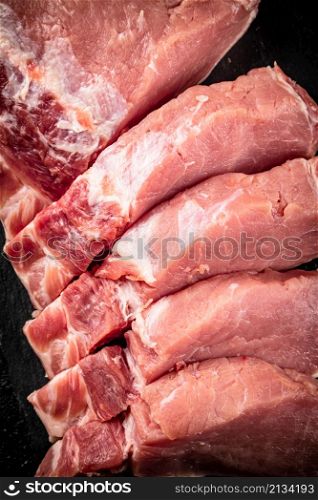 Pieces of raw pork on a stone board. On a black background. High quality photo. Pieces of raw pork on a stone board.