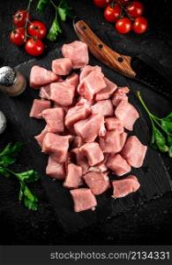 Pieces of raw pork on a stone board with parsley, tomatoes and spices. On a black background. High quality photo. Pieces of raw pork on a stone board with parsley, tomatoes and spices.
