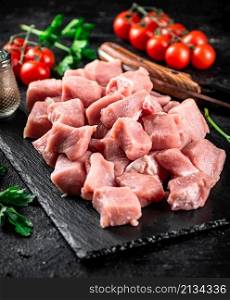 Pieces of raw pork on a stone board with parsley, tomatoes and spices. On a black background. High quality photo. Pieces of raw pork on a stone board with parsley, tomatoes and spices.