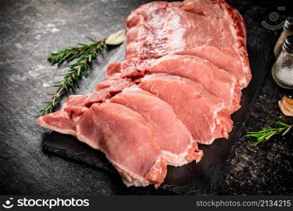 Pieces of raw pork on a stone board with rosemary and spices. On a black background. High quality photo. Pieces of raw pork on a stone board with rosemary and spices.