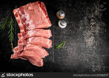 Pieces of raw pork on a stone board with rosemary and spices. On a black background. High quality photo. Pieces of raw pork on a stone board with rosemary and spices.