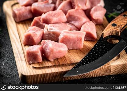 Pieces of raw pork on a wooden cutting board with a knife. On a black background. High quality photo. Pieces of raw pork on a wooden cutting board with a knife.