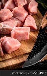 Pieces of raw pork on a wooden cutting board with a knife. On a black background. High quality photo. Pieces of raw pork on a wooden cutting board with a knife.
