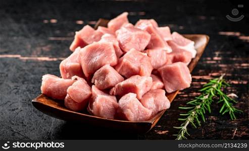 Pieces of raw pork on a wooden plate with a sprig of rosemary. Against a dark background. High quality photo. Pieces of raw pork on a wooden plate with a sprig of rosemary.