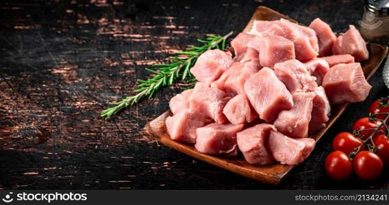 Pieces of raw pork on a wooden plate with a sprig of rosemary. Against a dark background. High quality photo. Pieces of raw pork on a wooden plate with a sprig of rosemary.
