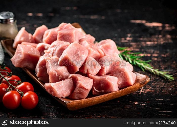 Pieces of raw pork on a wooden plate with spices and tomatoes. On a black background. High quality photo. Pieces of raw pork on a wooden plate with spices and tomatoes.