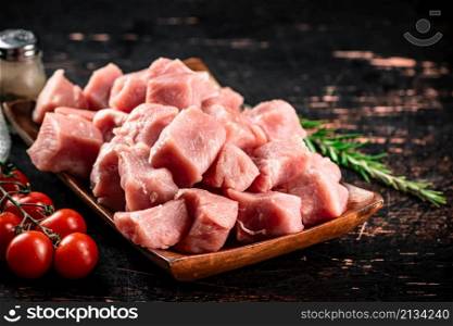 Pieces of raw pork on a wooden plate with spices and tomatoes. On a black background. High quality photo. Pieces of raw pork on a wooden plate with spices and tomatoes.