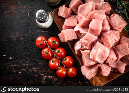 Pieces of raw pork on a wooden plate with spices and tomatoes. On a black background. High quality photo. Pieces of raw pork on a wooden plate with spices and tomatoes.