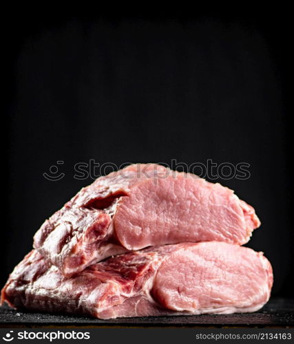 Pieces of raw pork on the table. On a black background. High quality photo. Pieces of raw pork on the table.