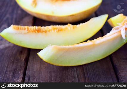 Pieces of ripe melon on a brown wooden table, close up