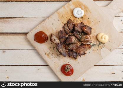 pieces of roasted meat with spices on a wooden tray with four kinds of sauces to meat