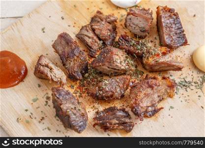 pieces of roasted meat with spices on a wooden tray with four kinds of sauces to meat