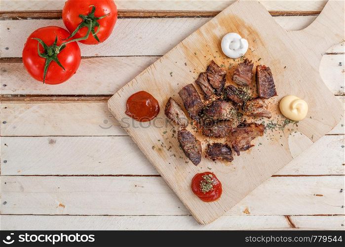 pieces of roasted meat with spices on a wooden tray with four kinds of sauces to meat and with tomatoes
