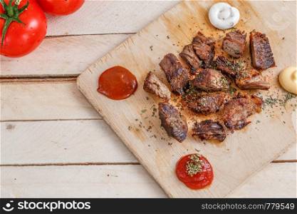 pieces of roasted meat with spices on a wooden tray with four kinds of sauces to meat and with tomatoes