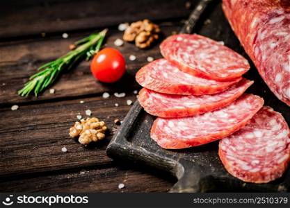 Pieces of salami sausage on a cutting board with cherry tomatoes and rosemary. On a wooden background. High quality photo. Pieces of salami sausage on a cutting board with cherry tomatoes and rosemary.