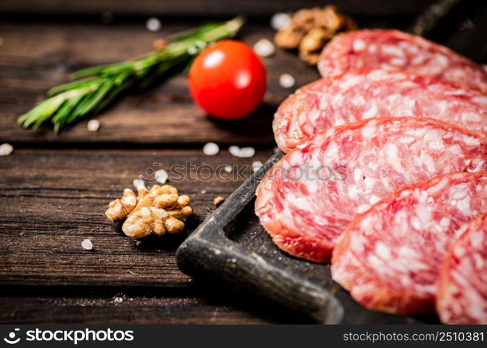 Pieces of salami sausage on a cutting board with cherry tomatoes and rosemary. On a wooden background. High quality photo. Pieces of salami sausage on a cutting board with cherry tomatoes and rosemary.