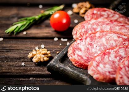 Pieces of salami sausage on a cutting board with cherry tomatoes and rosemary. On a wooden background. High quality photo. Pieces of salami sausage on a cutting board with cherry tomatoes and rosemary.