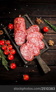 Pieces of salami sausage on a cutting board with cherry tomatoes and rosemary. On a wooden background. High quality photo. Pieces of salami sausage on a cutting board with cherry tomatoes and rosemary.