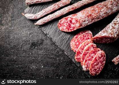 Pieces of salami sausage on a stone board. On a black background. High quality photo. Pieces of salami sausage on a stone board.
