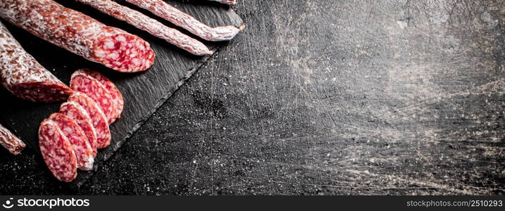 Pieces of salami sausage on a stone board. On a black background. High quality photo. Pieces of salami sausage on a stone board.