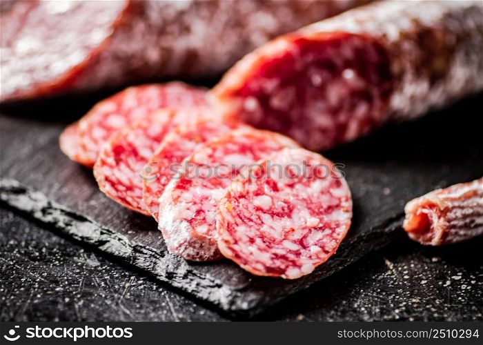 Pieces of salami sausage on a stone board. On a black background. High quality photo. Pieces of salami sausage on a stone board.