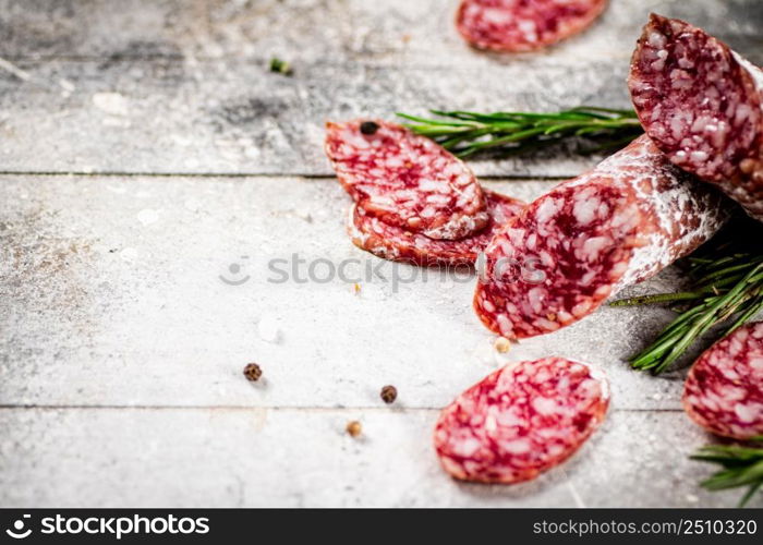 Pieces of salami sausage with sprigs of rosemary. On a gray background. High quality photo. Pieces of salami sausage with sprigs of rosemary.