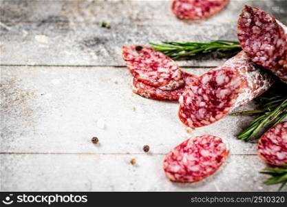 Pieces of salami sausage with sprigs of rosemary. On a gray background. High quality photo. Pieces of salami sausage with sprigs of rosemary.