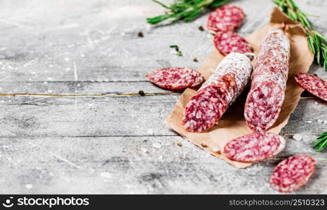 Pieces of salami sausage with sprigs of rosemary. On a gray background. High quality photo. Pieces of salami sausage with sprigs of rosemary.
