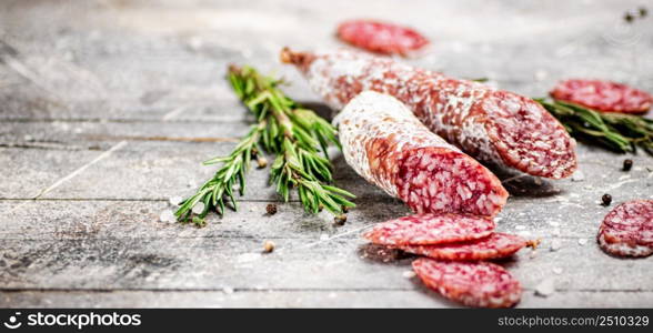 Pieces of salami sausage with sprigs of rosemary. On a gray background. High quality photo. Pieces of salami sausage with sprigs of rosemary.