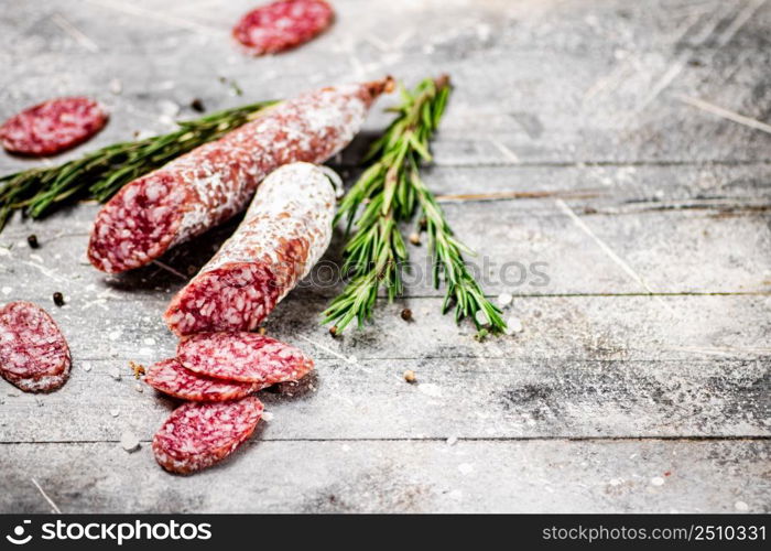 Pieces of salami sausage with sprigs of rosemary. On a gray background. High quality photo. Pieces of salami sausage with sprigs of rosemary.