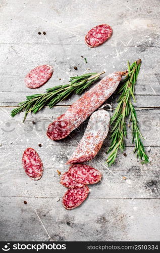 Pieces of salami sausage with sprigs of rosemary. On a gray background. High quality photo. Pieces of salami sausage with sprigs of rosemary.