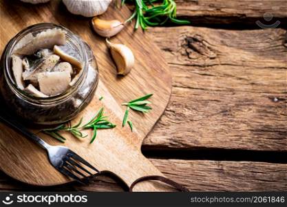 Pieces of salted herring in a glass jar on a cutting board. On a wooden background. High quality photo. Pieces of salted herring in a glass jar on a cutting board.